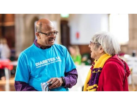 A man in a blue Diabetes UK shirt engages in conversation with a woman wearing a colorful scarf at an event.